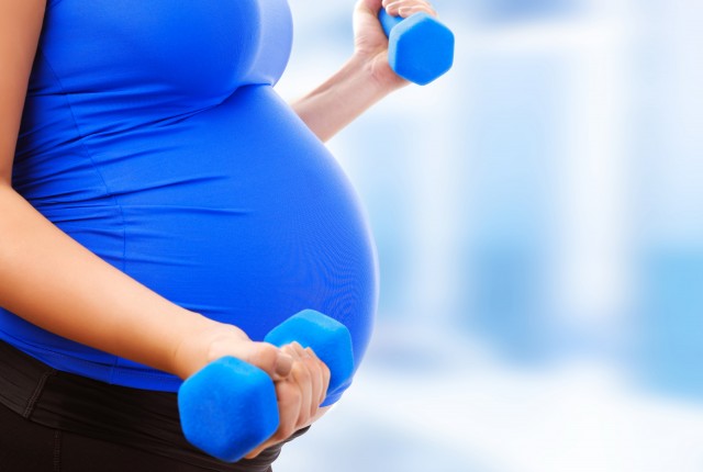 Pregnant female do exercise in sports hall, side view, body part, lifting dumbbells, active and sportive pregnancy, healthy motherhood concept